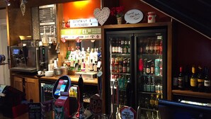 A bar area with a coffee machine, a cash register, and a variety of bottles and glasses on shelves. - The Mount By Greene King Inns (Wigan)