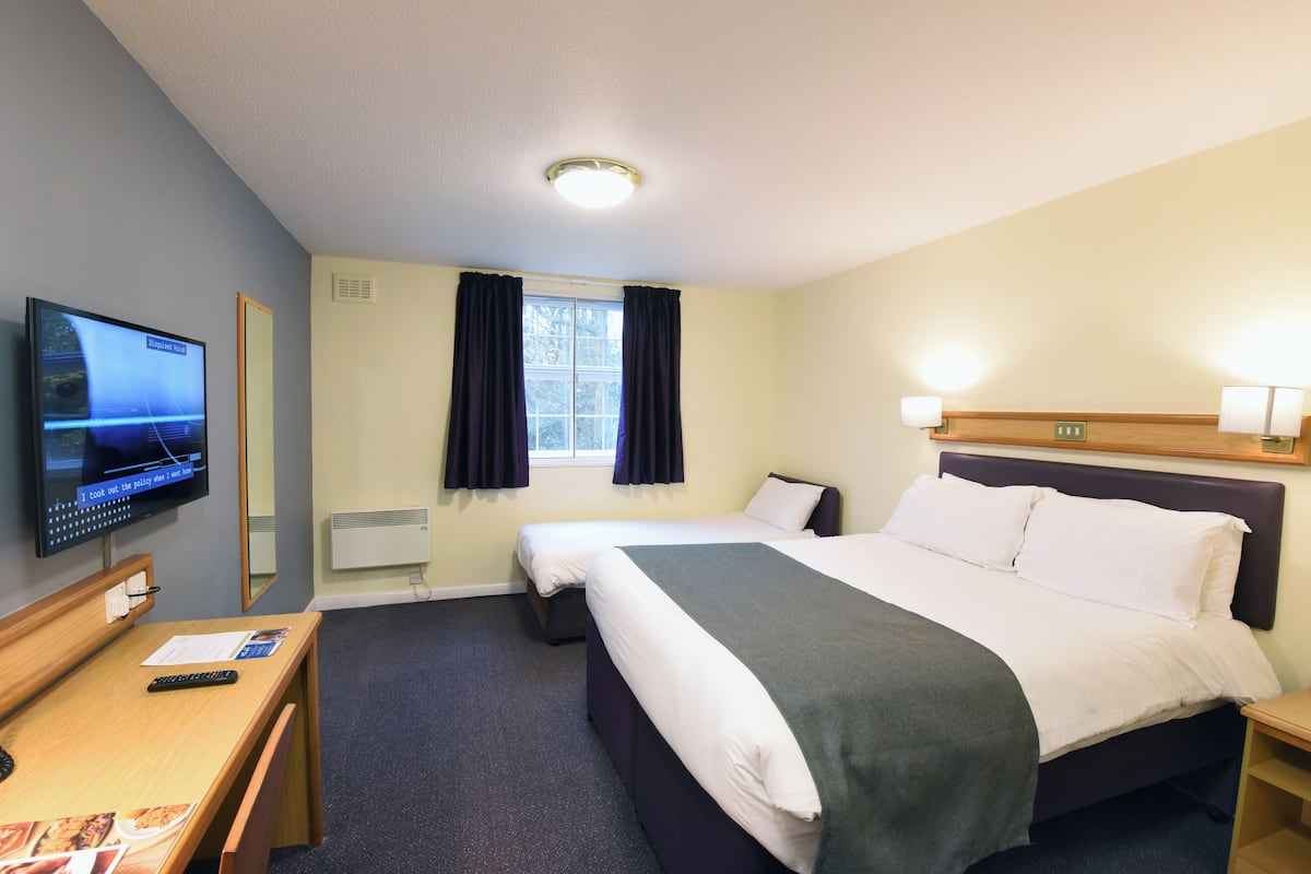 Ein Hotelzimmer mit Bett, Schreibtisch mit Stuhl, Fernseher und einem Fenster mit Vorhängen.