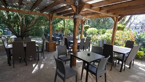 An outdoor patio with tables and chairs, covered by a wooden pergola, surrounded by greenery. - The Mount By Greene King Inns (Wigan)