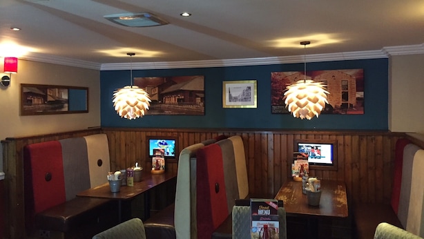 A restaurant with booths and tables, wooden paneling, hanging pendant lights, and wall-mounted televisions. - The Mount By Greene King Inns (Wigan)