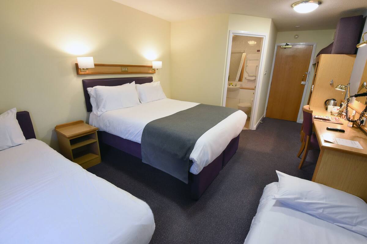 Ein Hotelzimmer mit zwei Betten, einem Schreibtisch, einem Stuhl, einem Kleiderschrank und einem Badezimmer.