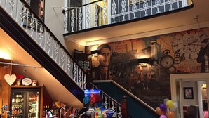 A bar area with a counter, a staircase with decorative railings, and a mural on the wall. - The Mount By Greene King Inns (Wigan)