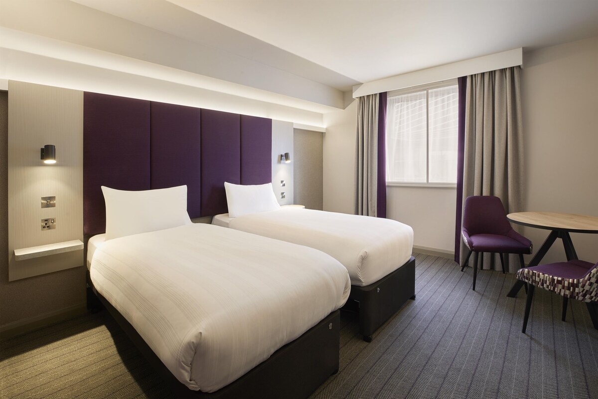 A hotel room with two beds, a desk, a chair, and a window with curtains.
