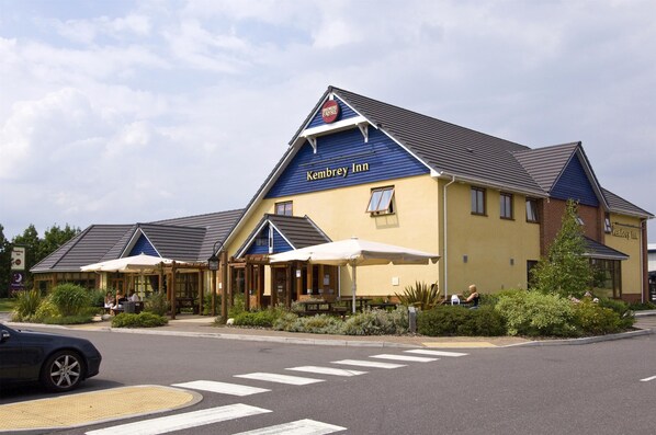 Un établissement Kembrey Inn à l’extérieur bleu et jaune, doté d’une terrasse et d’un passage piéton devant l’entrée.