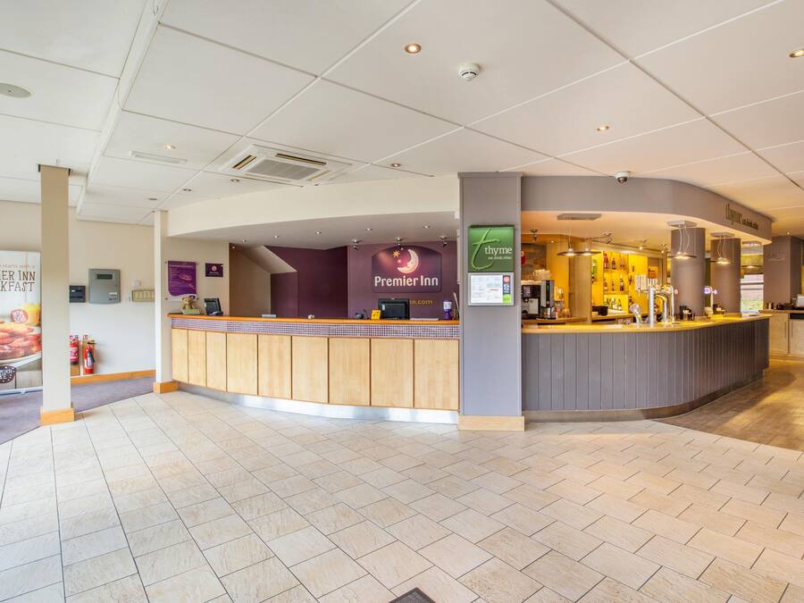 Un espace d’accueil d’hôtel avec un comptoir, un panneau indiquant « Premier Inn » et un restaurant appelé « Thyme ».