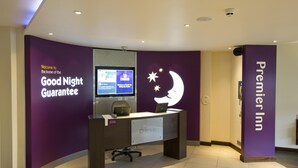 Una reception hotel con un cartello che indica la 'Good Night Guarantee', un computer e un cartello con il marchio 'Premier Inn'.