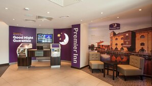 A Premier Inn reception area with a check-in counter, self-service machines, a seating area with a mural, and a 'Good Night Guarantee' sign. - Premier Inn Wigan Town Centre (Wigan)
