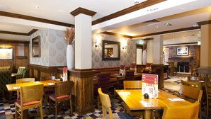A restaurant with wooden furniture, patterned wallpaper, and a fireplace. - Premier Inn Glastonbury (Glastonbury)