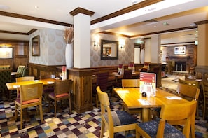 A restaurant with wooden furniture, patterned wallpaper, and a fireplace. - Premier Inn Glastonbury (Glastonbury)