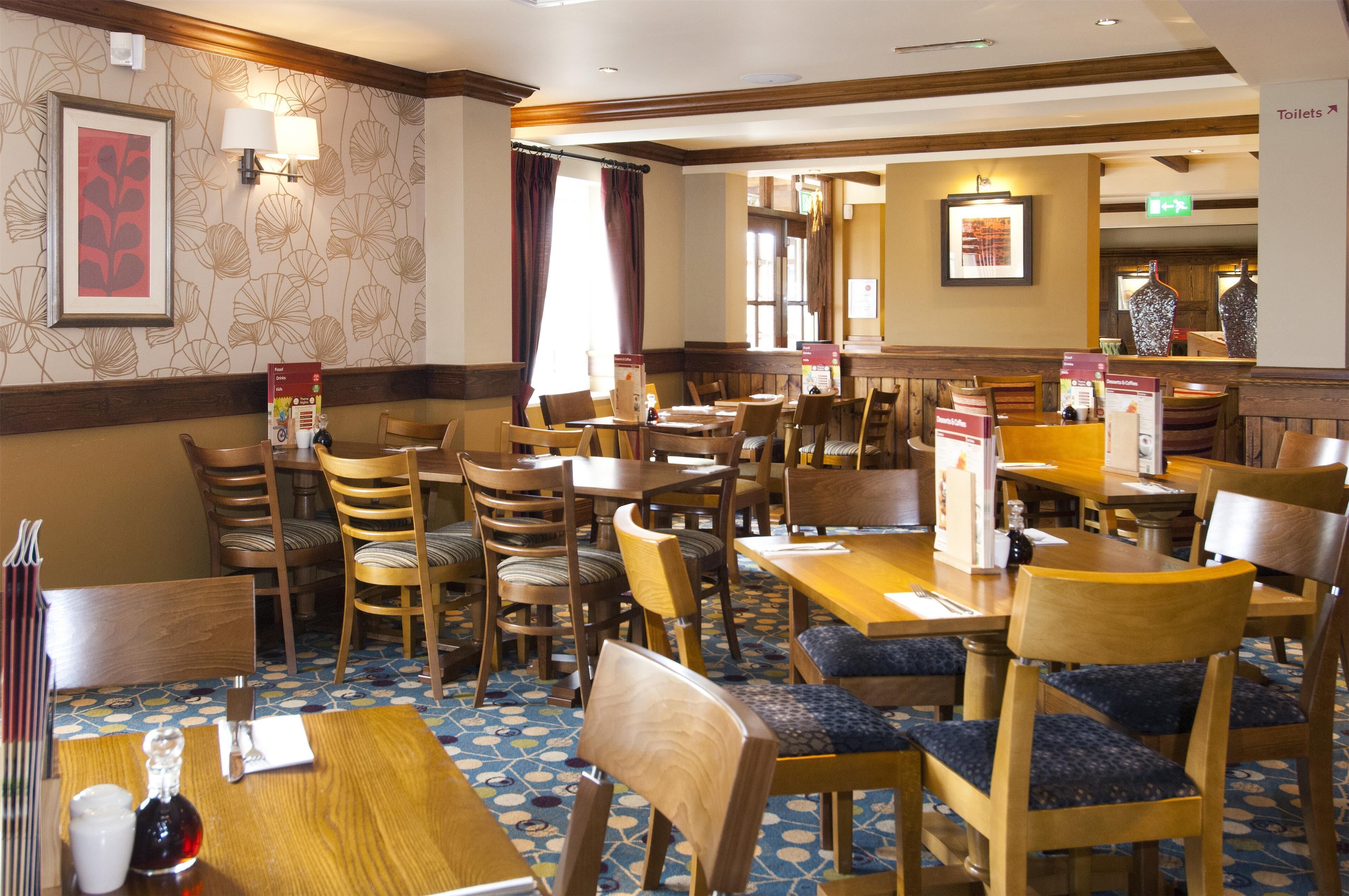 A restaurant with wooden tables and chairs, framed artwork on the walls, and a patterned floor.