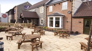 A brick building with outdoor seating and a sign for 'Premier's Favre.' - Premier Inn Glastonbury (Glastonbury)