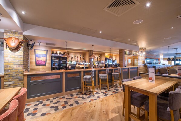 A bar area with a counter, stools, and a variety of bottles.