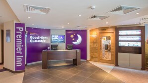 Ein Hotel-Empfangsbereich mit lila Wand, einer Rezeption, einer Uhr und einem Schild für Premier Inn.