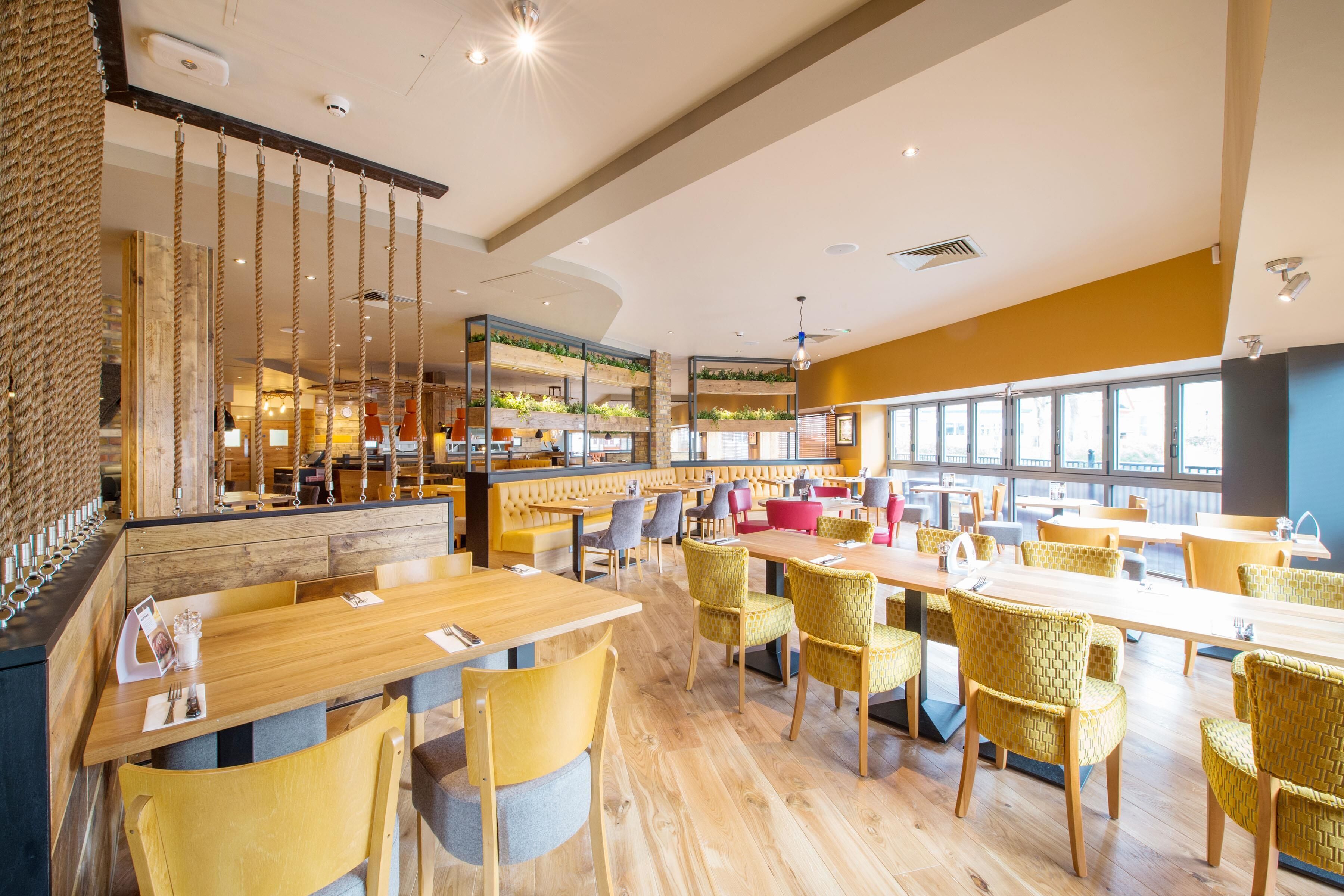 A spacious restaurant with high ceilings, wooden tables, and yellow chairs.