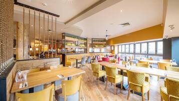A spacious restaurant with high ceilings, wooden tables, and yellow chairs.