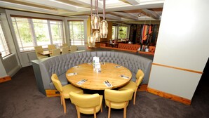 Une table ronde entourée de six chaises, un coin bar et de grandes fenêtres équipées de stores.