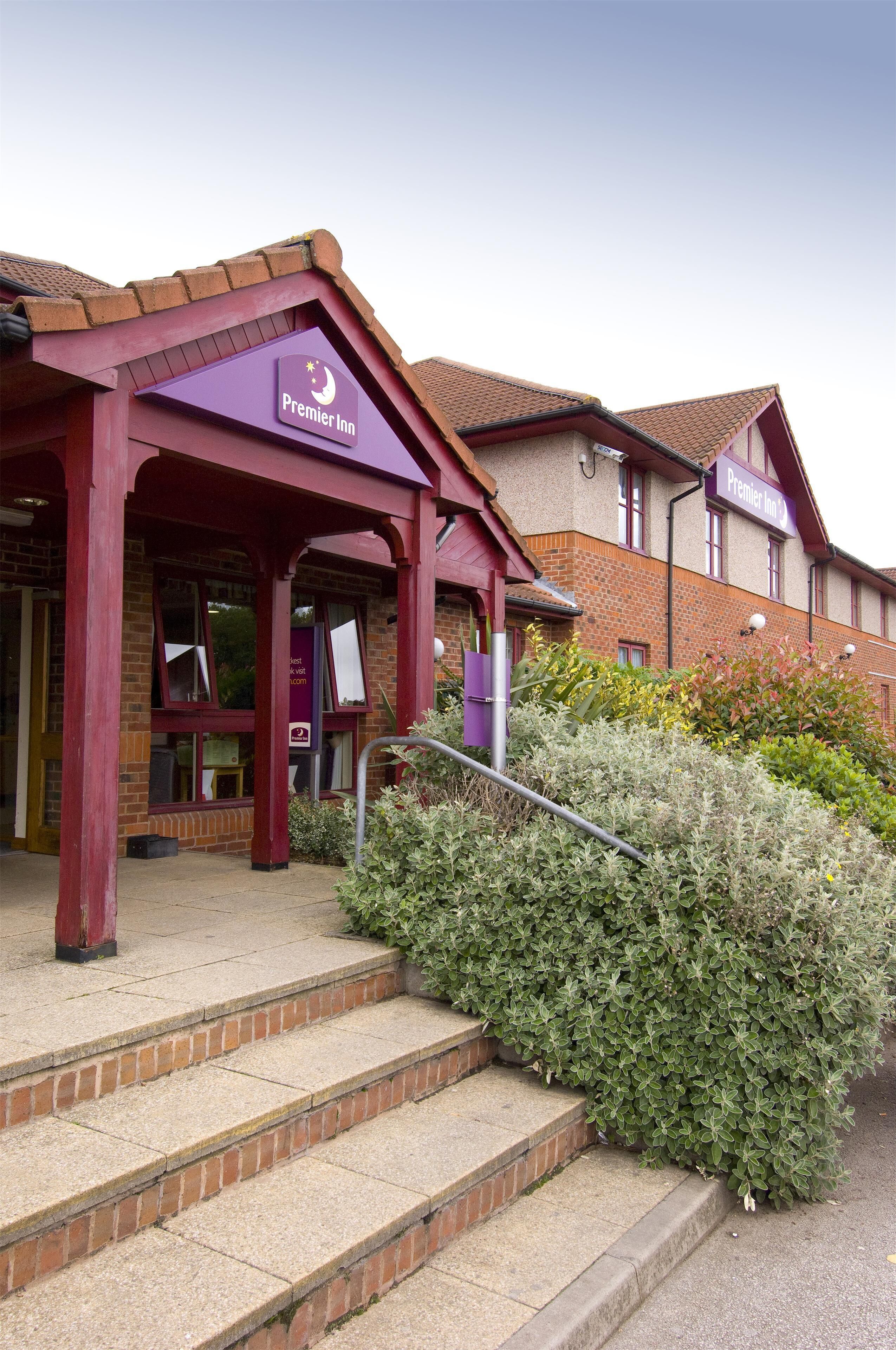 A hotel entrance with a sign reading 'Premier Inn,' a brick facade, and a set of steps leading to the entrance.