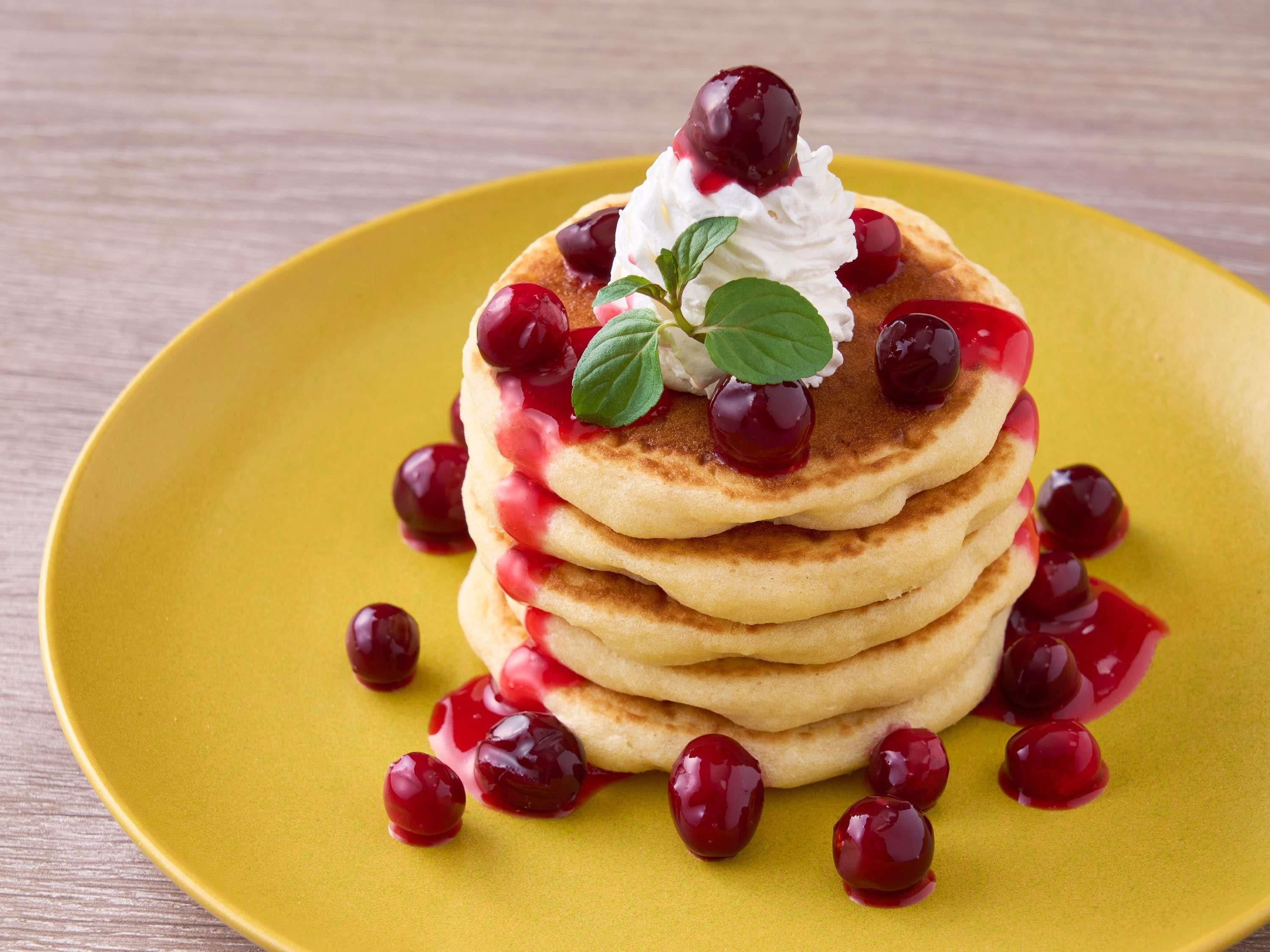 Une pile de crêpes garnies de cerises et de crème fouettée, servies dans une assiette jaune.