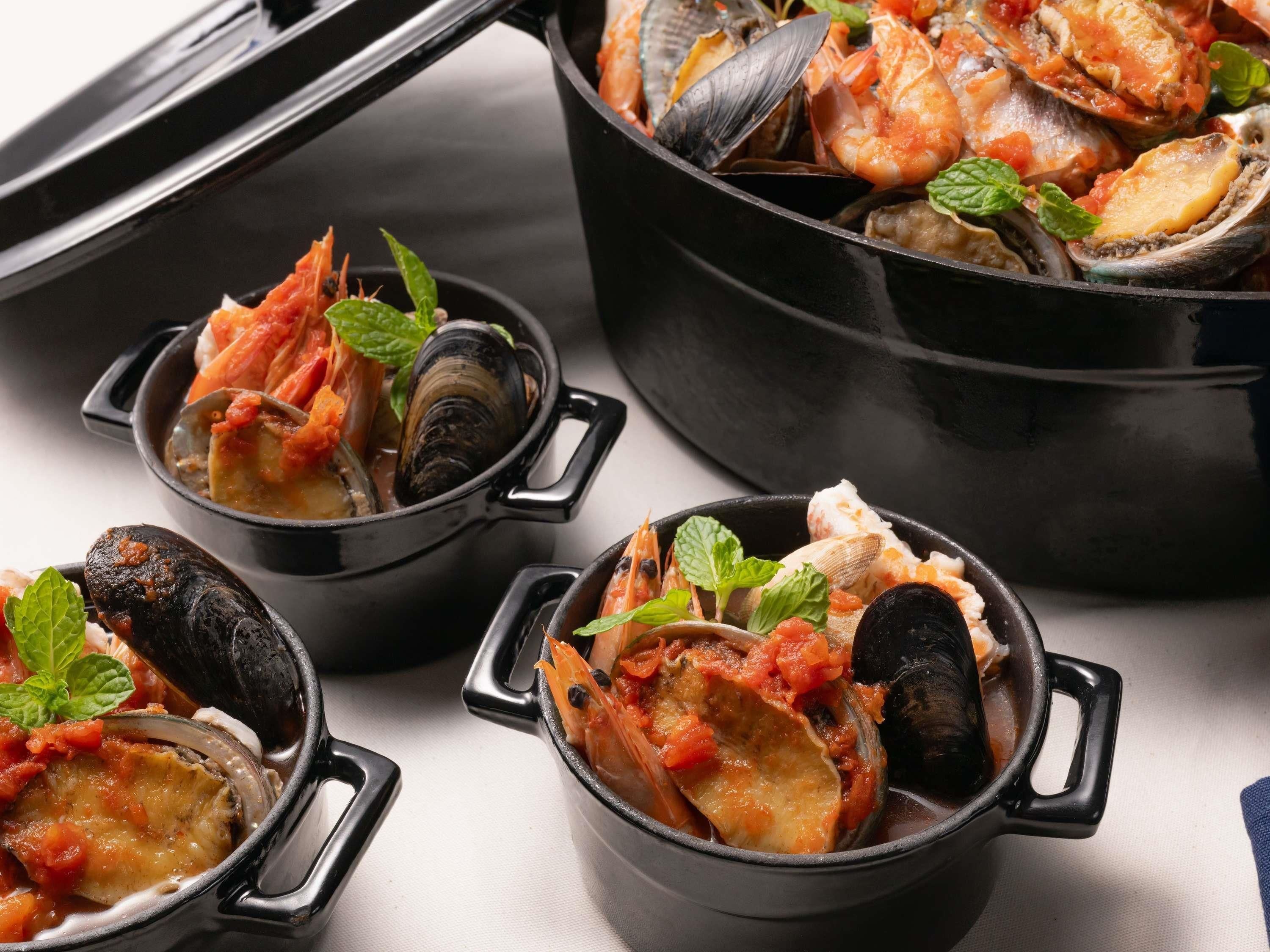 A seafood dish in a black pot with handles, accompanied by smaller bowls containing similar seafood.