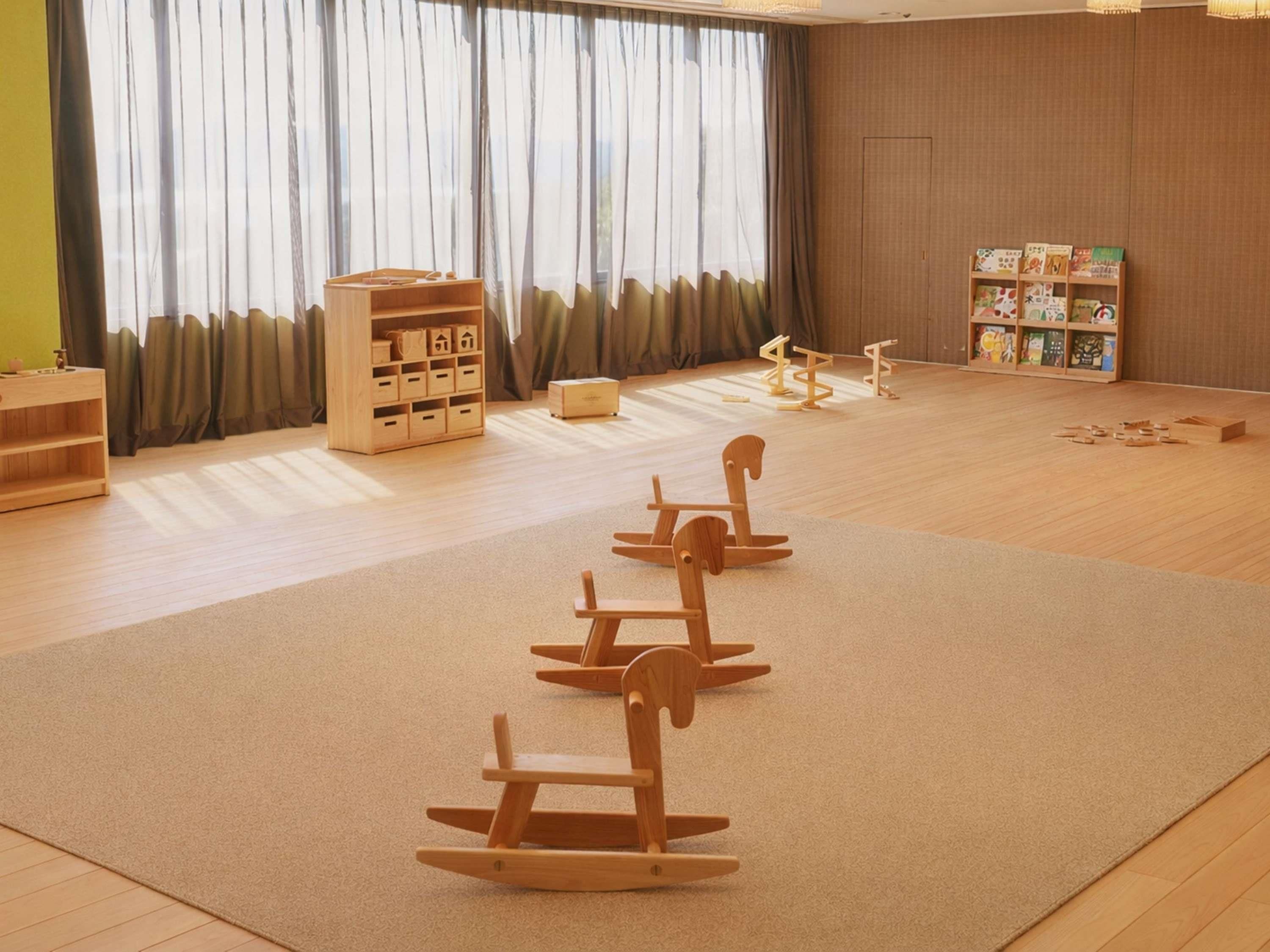 A spacious room with a large window, wooden play area, storage units, and a bookshelf.
