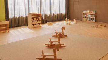 A spacious room with a large window, wooden play area, storage units, and a bookshelf.