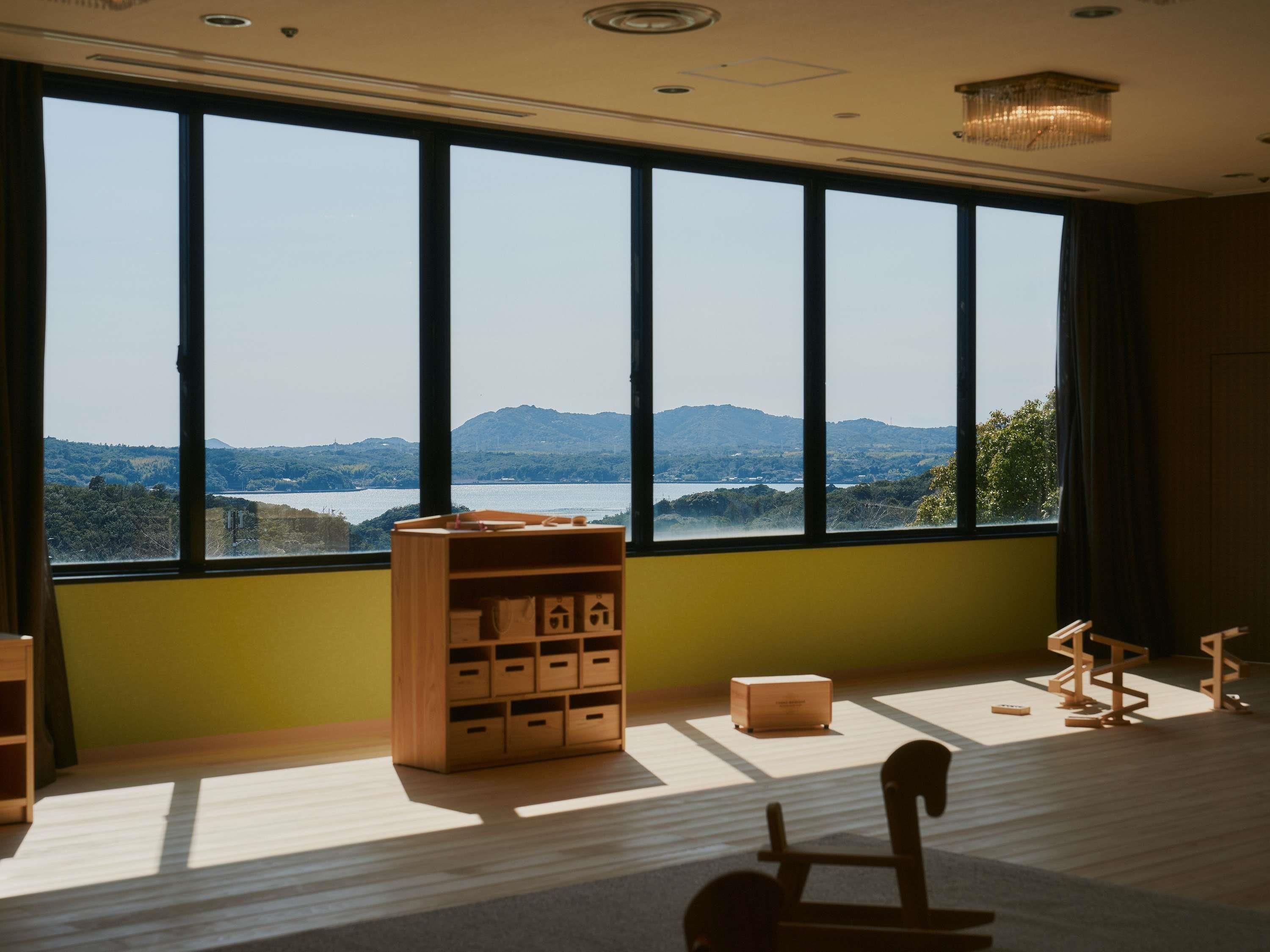 A room with large windows, a wooden play area, and a view of a lake and hills.