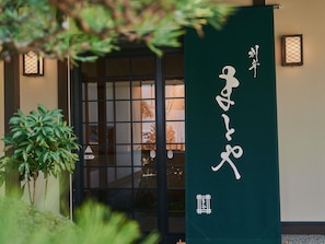 A traditional Japanese building entrance with a sliding door, a green banner with white characters, and a small lantern on the wall. - Grand Mercure Ise-shima Resort & Spa (Shima)
