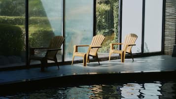 Un interno moderno con parete in vetro, due sedie in legno e un elemento d'acqua riflettente.