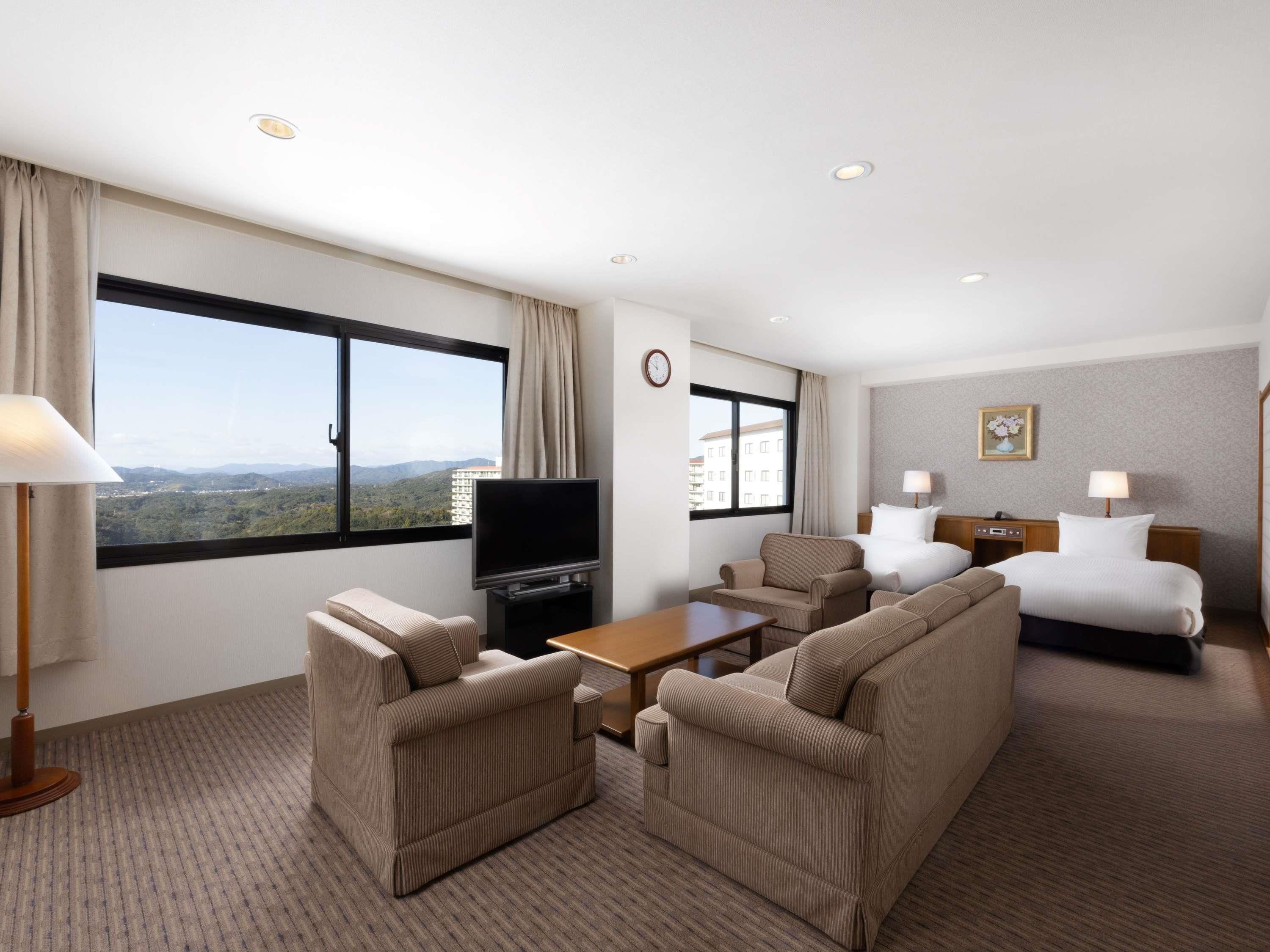 A hotel room with a large window, a flat-screen TV, a sofa, a bed, and a small table.