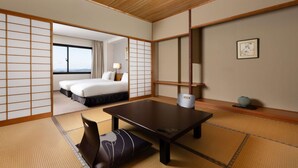 A traditional Japanese-style room with tatami flooring, a low table, and a bed with a view. - Grand Mercure Ise-shima Resort & Spa (Shima)