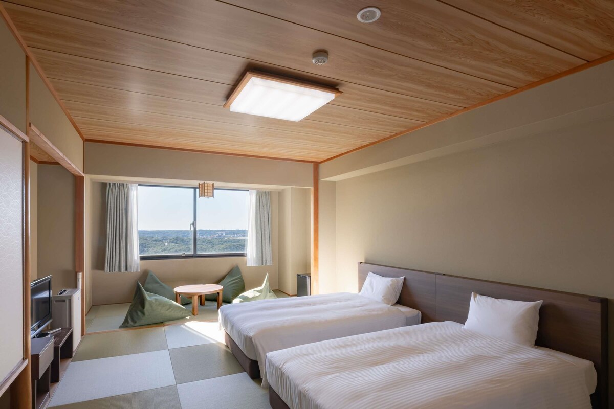 Habitación de hotel con dos camas, un televisor, una mesita y vista a la ciudad.