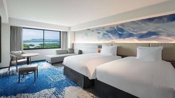 A hotel room with a large bed, a smaller bed, a sofa, a chair, and a table. There is a large window with a view of a landscape.