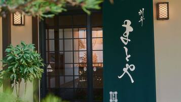 A traditional Japanese building entrance with a sliding door, a green banner with white characters, and a small lantern on the wall.