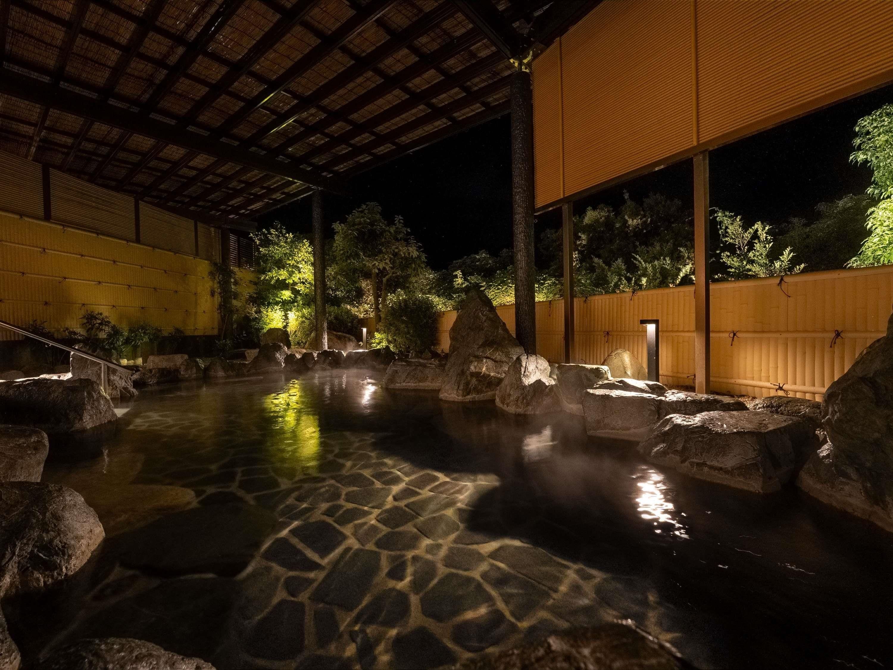 Un espace de sources chaudes naturelles, avec des pierres, une terrasse en bois et un abri couvert.