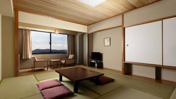 A traditional Japanese room with tatami flooring, a low table, a sofa, a TV, and a window with a view.