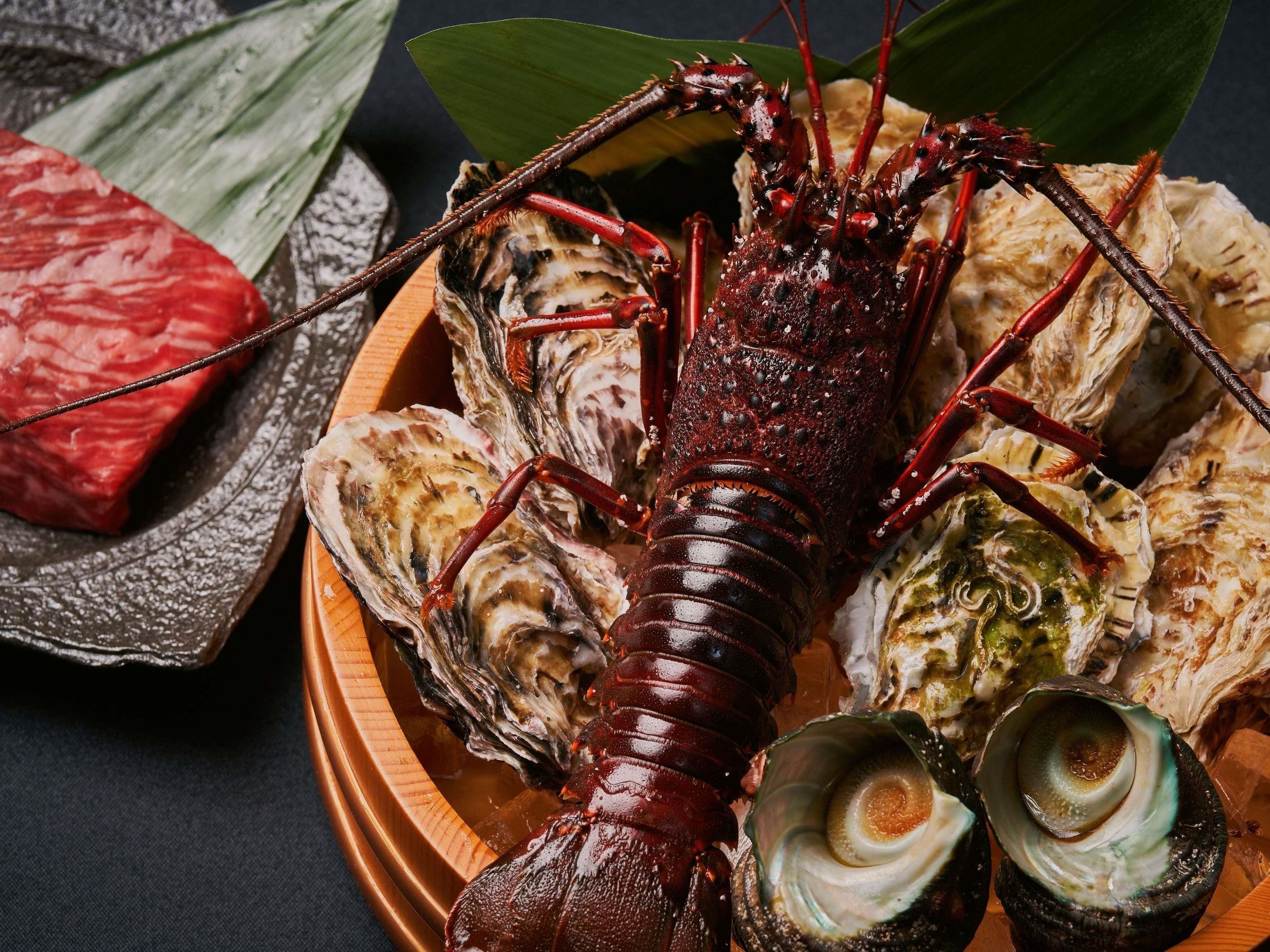 A lobster with a plate of oysters and a piece of red meat.