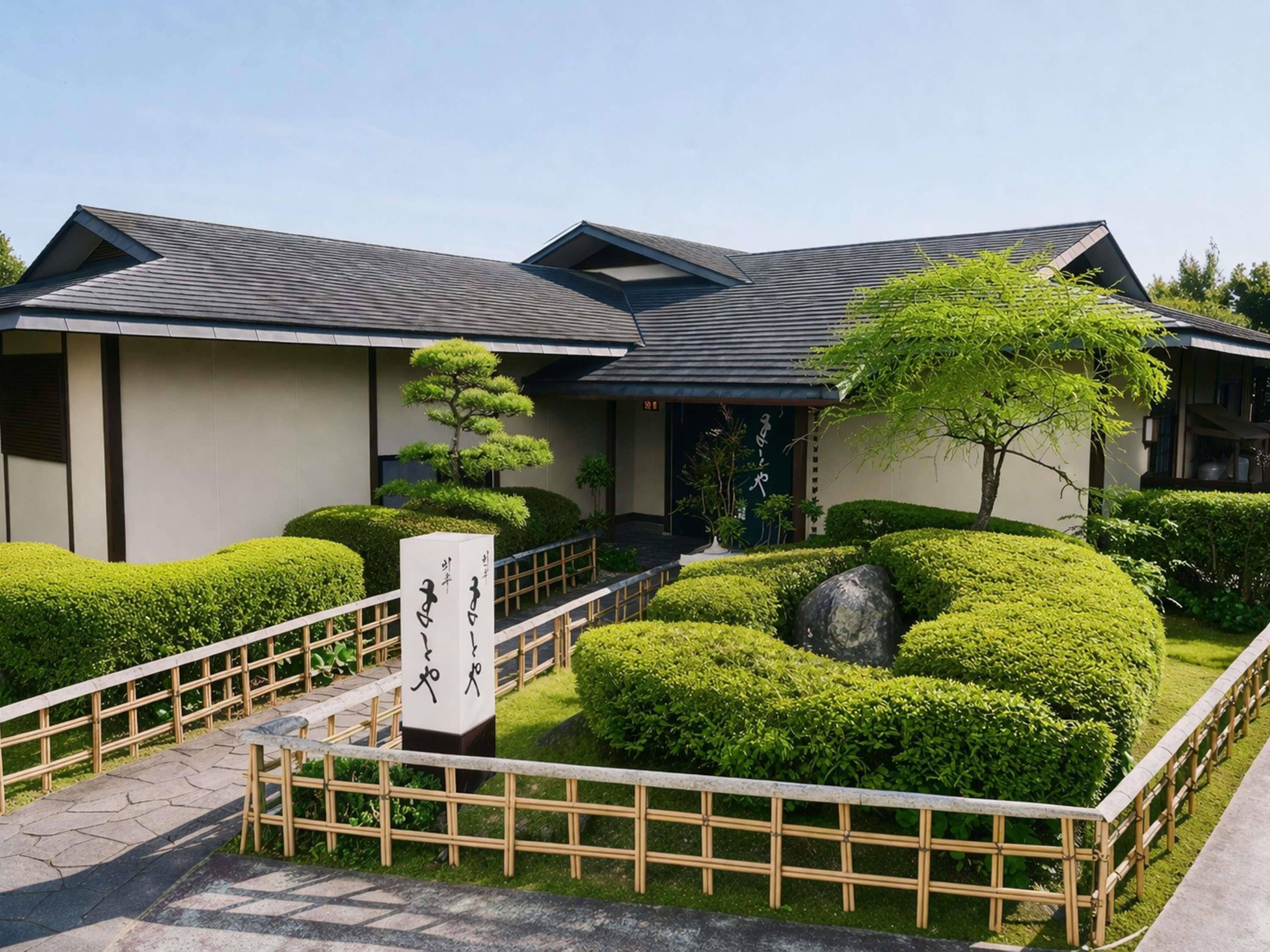 Ein traditionelles japanisches Gebäude mit einem Ziegeldach, einem Holzzaun und gepflegter Bepflanzung.