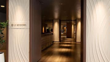 A hotel entrance with a modern design, a reception desk, and a sign reading 'LE SENSORIEL'.