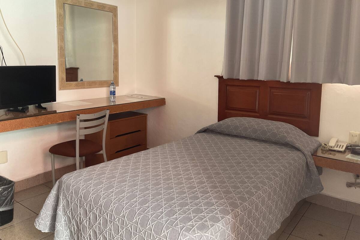 A bedroom with a bed, a desk with a computer, a chair, a mirror, and a telephone.