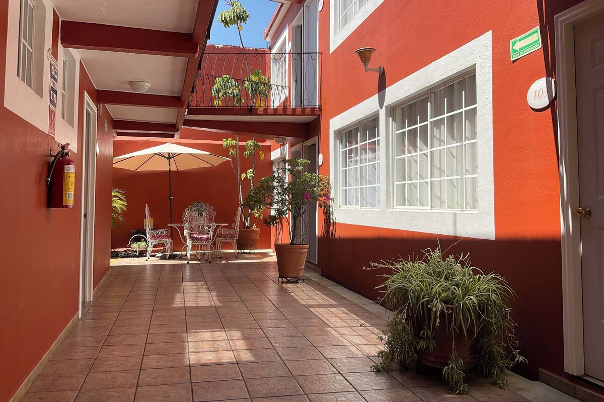 A corridor with a tiled floor, a fire extinguisher, a table with chairs, and potted plants.
