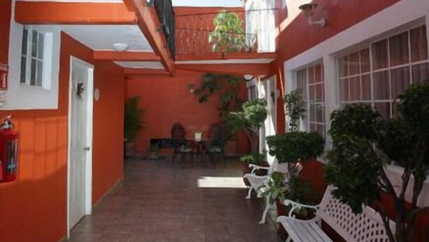 Un espacio al aire libre cubierto, con suelo de baldosas, bancos blancos y plantas en macetas.