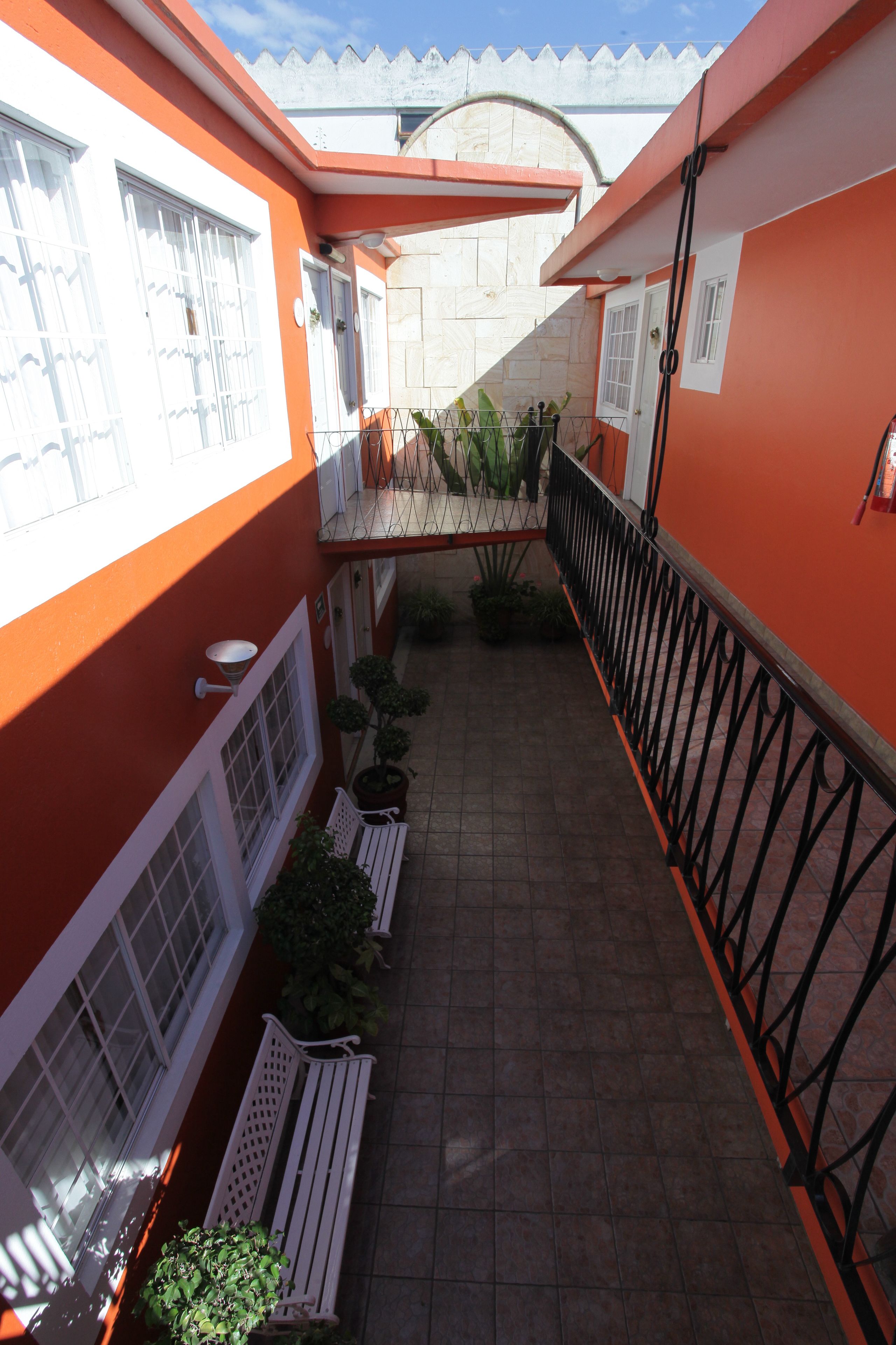 A narrow outdoor corridor with orange walls, white railings, and potted plants.