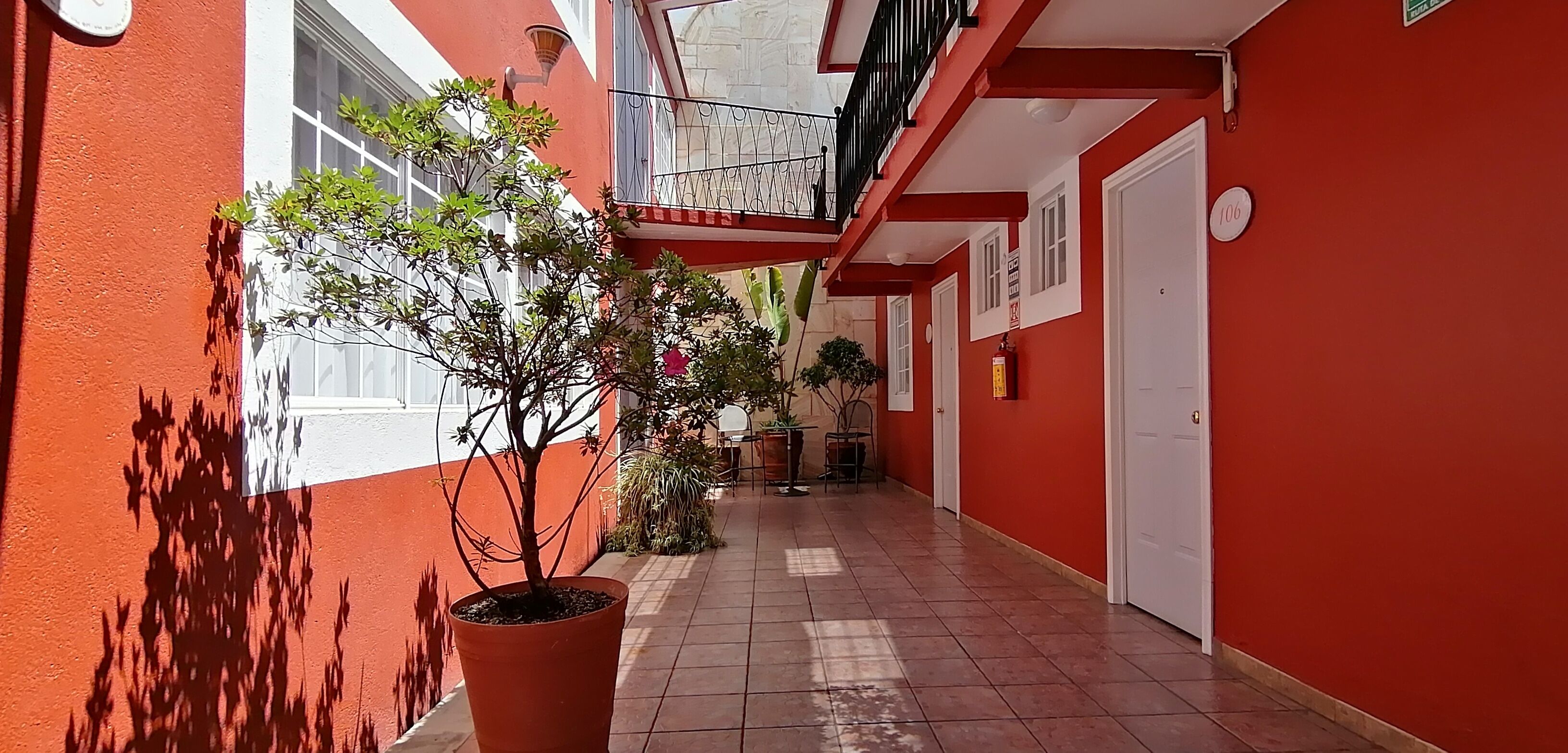 A narrow corridor with red walls, a potted plant, and a door marked with the number 106.