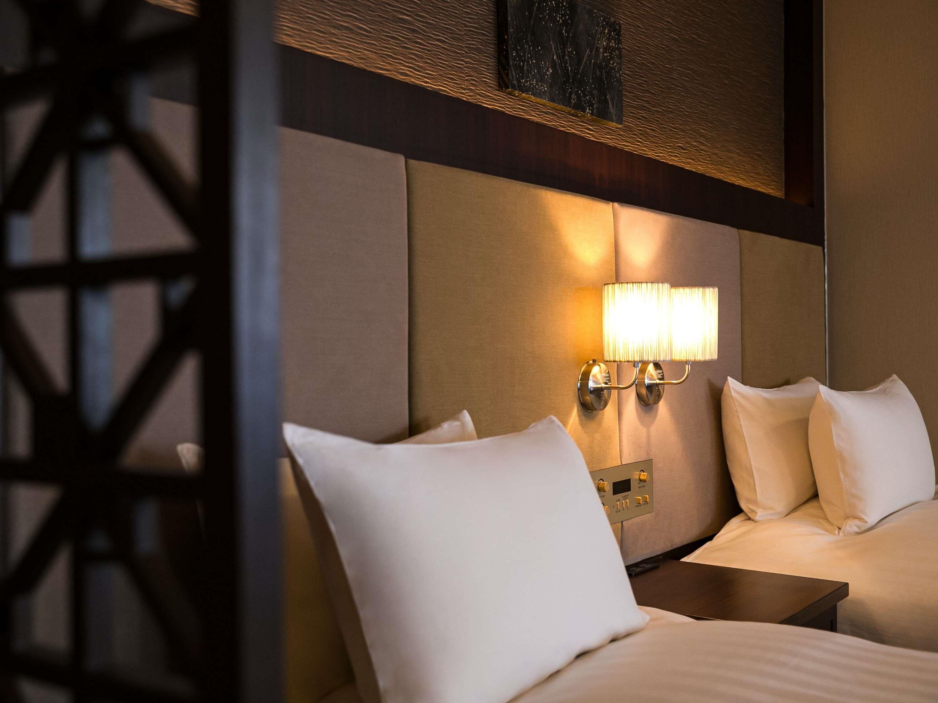 Une chambre d’hôtel avec un lit, une table de chevet et une lampe fixée au mur.