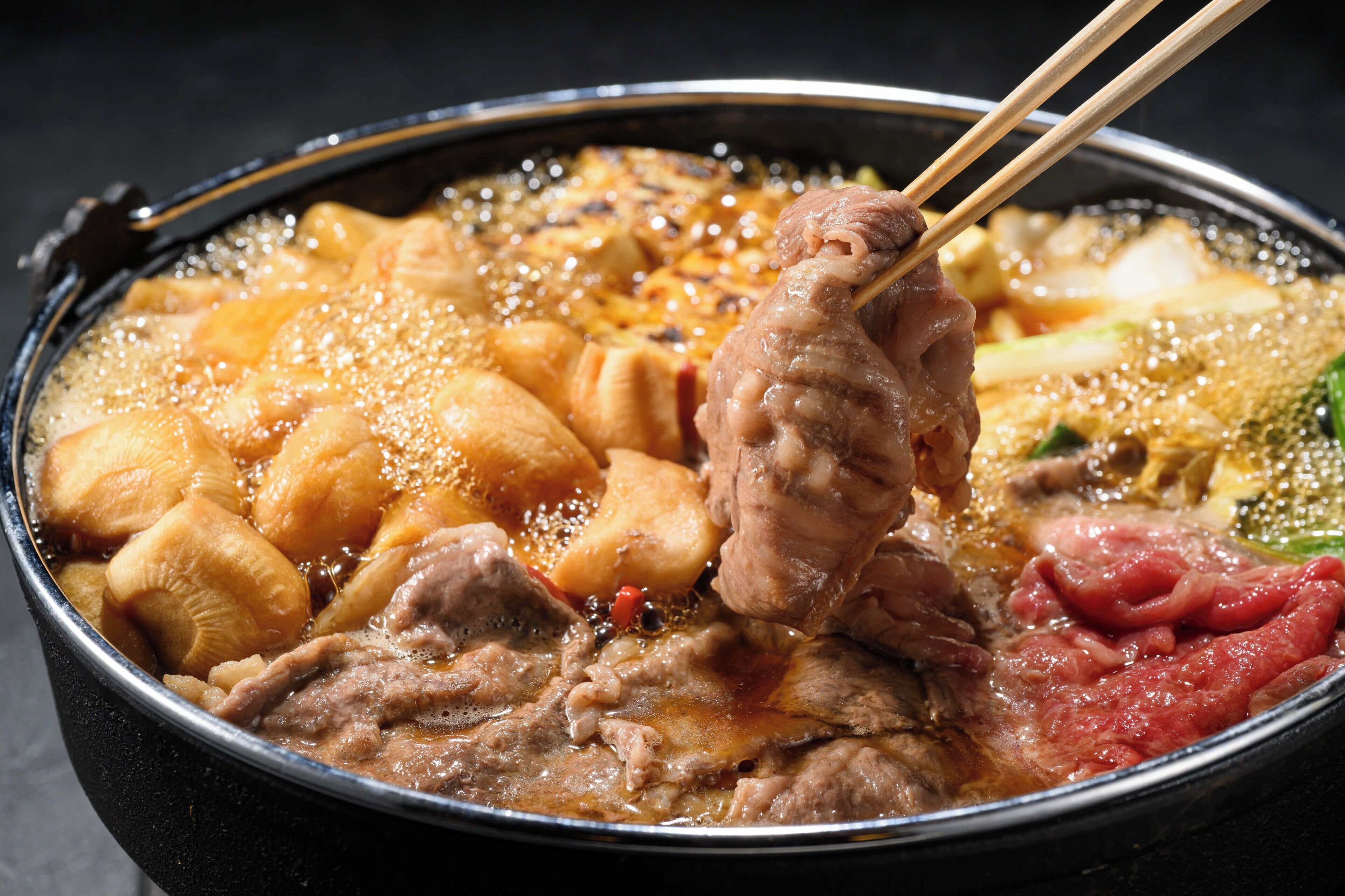 Primer plano de un plato de olla caliente con diversos ingredientes servidos en palillos.
