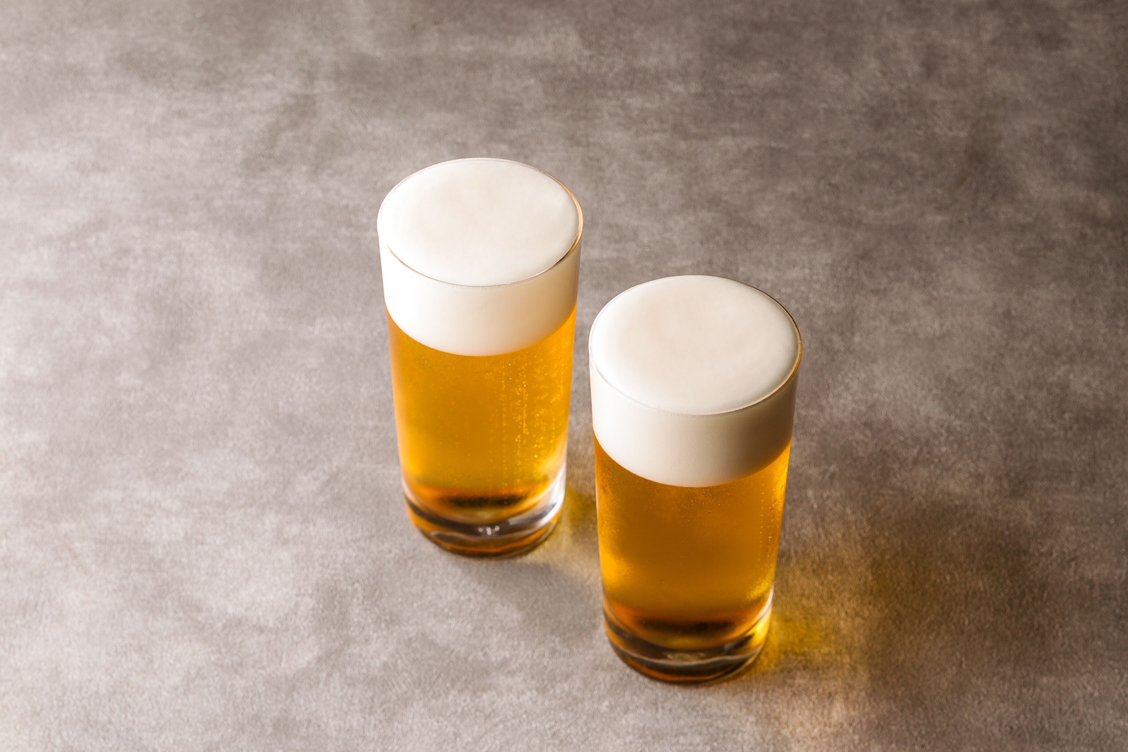 Two glasses of beer on a textured surface.