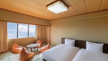 A hotel room with a bed, two pillows, a round table, and a view of the sky through large windows.