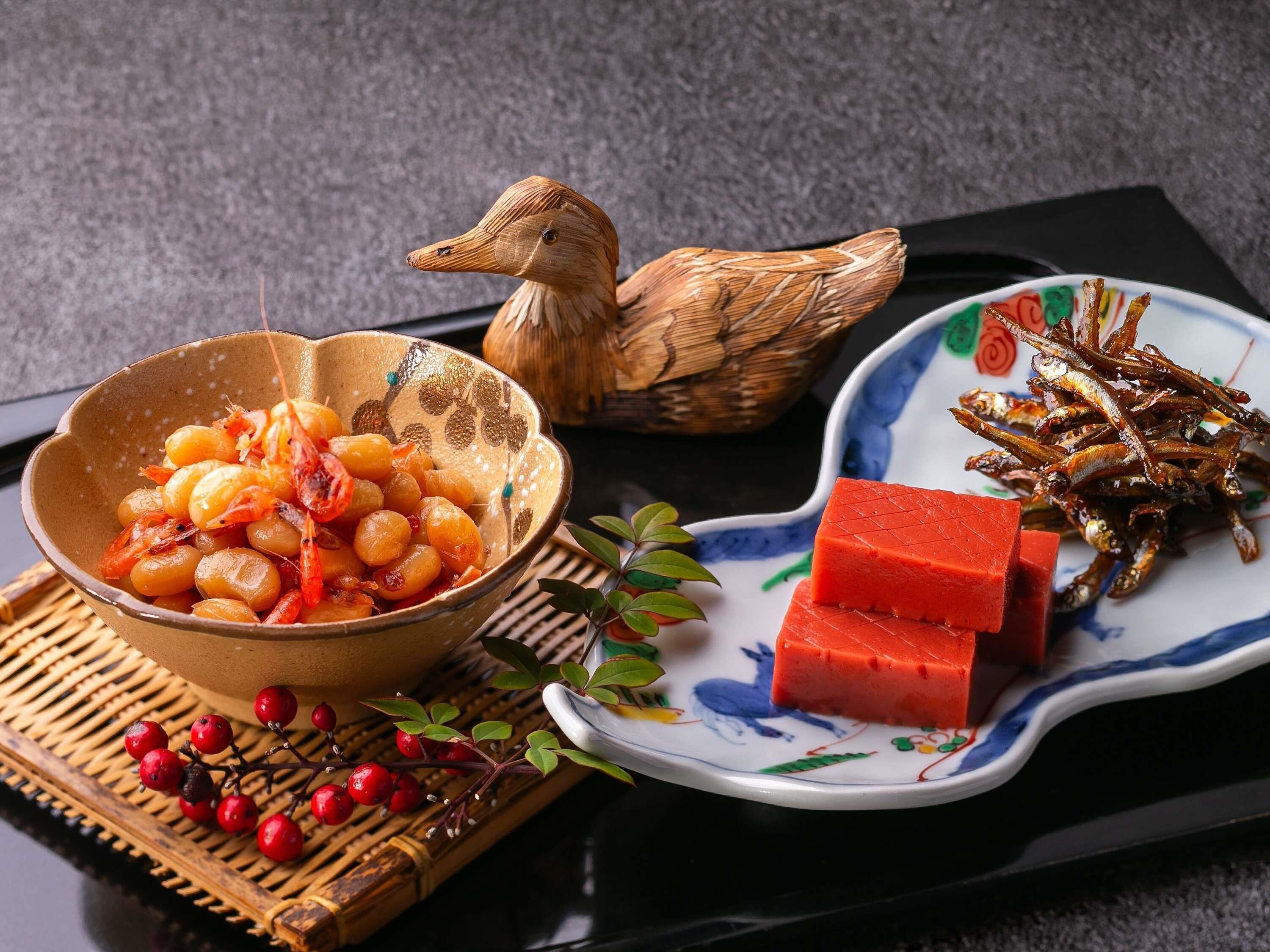 A table with a bowl of cooked shrimp, a plate of red cubes, and fried fish.