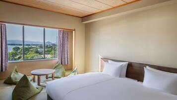 Habitación de hotel con una cama grande, una mesita redonda y vistas a un lago y montañas.