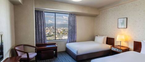 A hotel room with a large window, a bed, a desk with a chair, and a bedside table with a lamp.